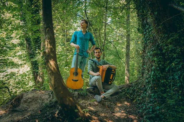 Press photo: Timmy with his guitar and Jonny with his Styrian accordion in a sunlit forest